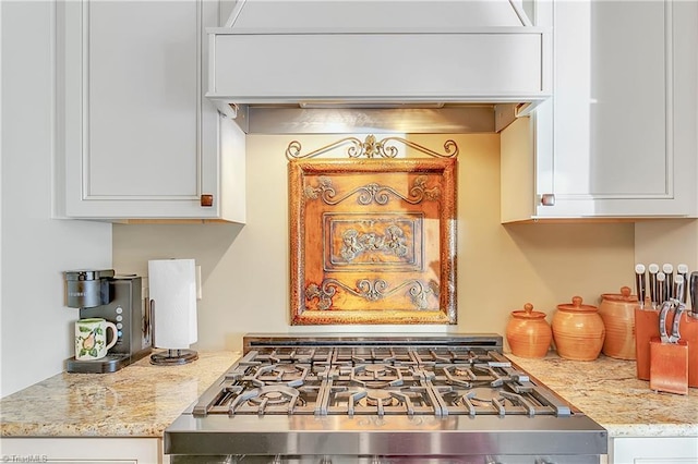 kitchen with custom range hood, light stone countertops, range, and white cabinets