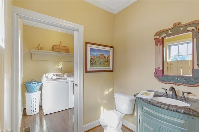 half bathroom with toilet, washer and dryer, wood finished floors, crown molding, and vanity