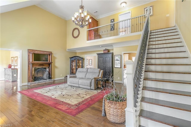 living room with stairs, hardwood / wood-style floors, a fireplace, an inviting chandelier, and high vaulted ceiling