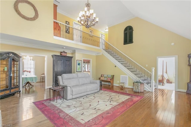 living area with stairs, ornamental molding, wood finished floors, and a chandelier