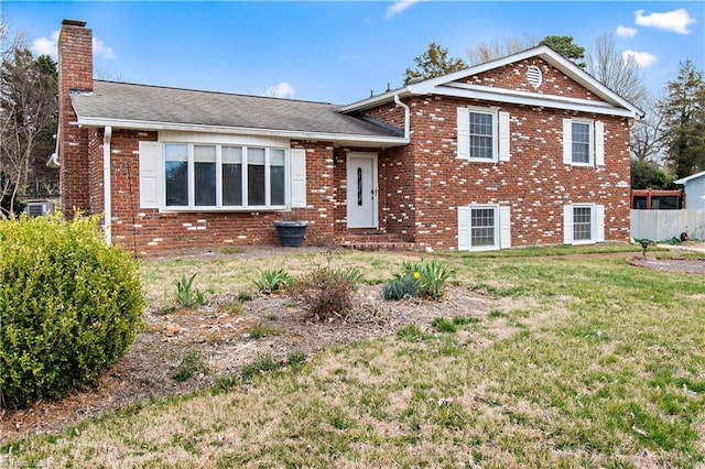 tri-level home with brick siding, a chimney, a front yard, and fence