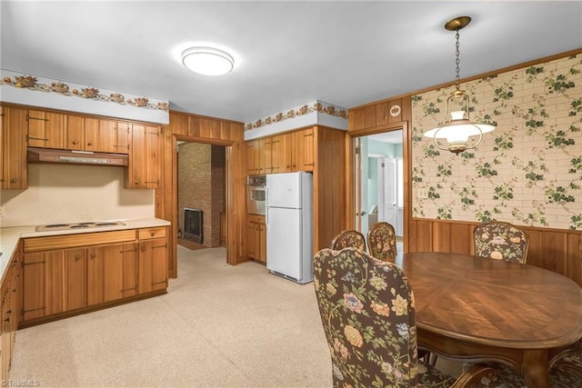 kitchen featuring white appliances, light countertops, a wainscoted wall, wallpapered walls, and under cabinet range hood