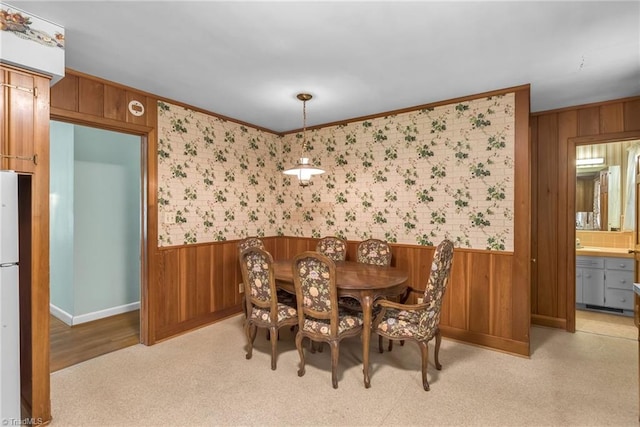 dining room with wooden walls, baseboards, ornamental molding, and a wainscoted wall