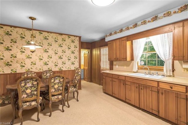 kitchen with a sink, light countertops, brown cabinets, and wallpapered walls