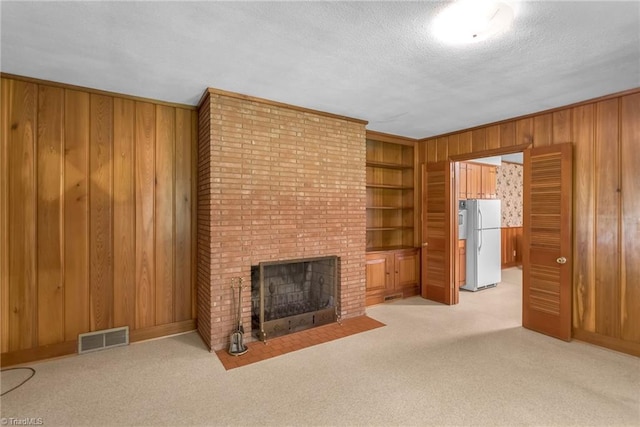 unfurnished living room featuring visible vents, wood walls, a fireplace, built in shelves, and carpet
