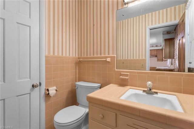 bathroom featuring toilet, wallpapered walls, wainscoting, and vanity