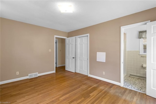 unfurnished bedroom featuring light wood-style floors, baseboards, a closet, and visible vents