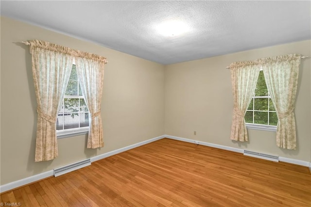 unfurnished room with baseboards, visible vents, a healthy amount of sunlight, and wood finished floors