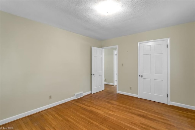 unfurnished bedroom featuring baseboards, light wood finished floors, a textured ceiling, and visible vents