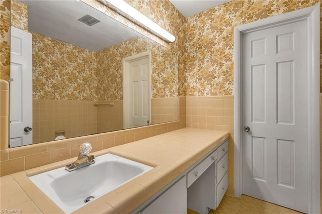 bathroom with wallpapered walls, tile walls, wainscoting, and vanity