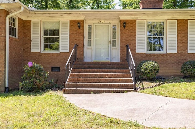 doorway to property with a chimney, a yard, and brick siding