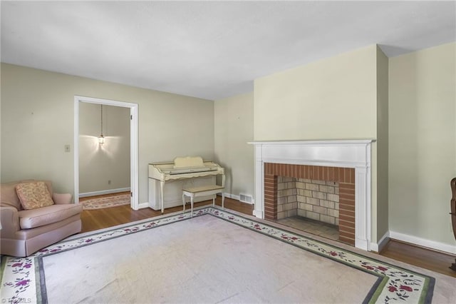 living area featuring baseboards, a fireplace, wood finished floors, and visible vents