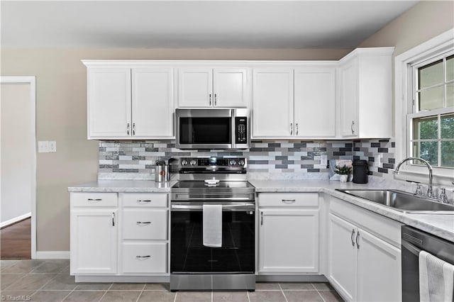 kitchen with sink, light tile patterned floors, appliances with stainless steel finishes, white cabinetry, and tasteful backsplash