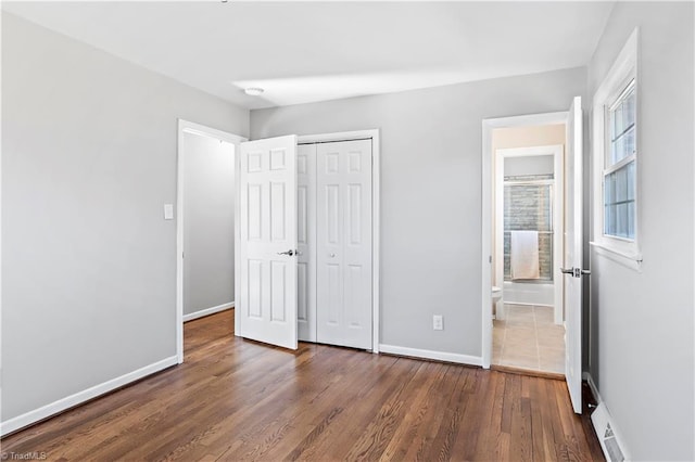 unfurnished bedroom with ensuite bathroom, dark hardwood / wood-style floors, and a closet