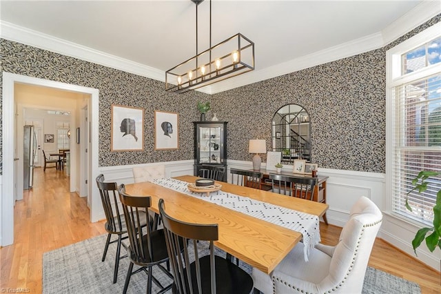 dining room featuring ornamental molding, a healthy amount of sunlight, wainscoting, and wallpapered walls