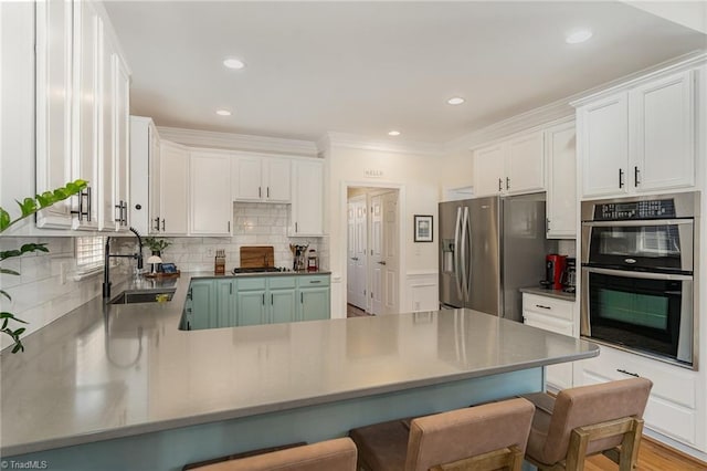 kitchen featuring stainless steel appliances, a peninsula, a sink, white cabinetry, and a kitchen bar