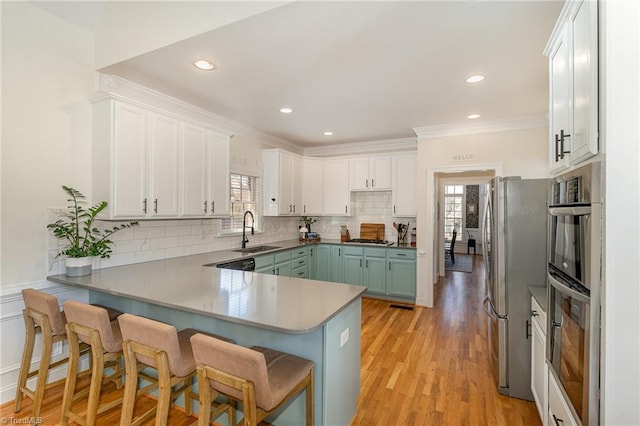 kitchen with a peninsula, stainless steel appliances, a kitchen bar, white cabinetry, and a sink