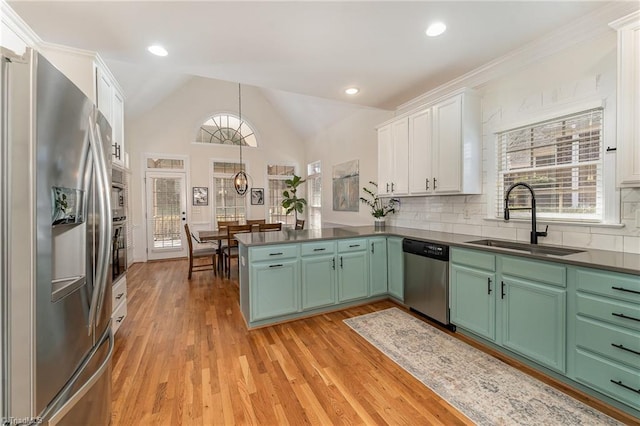 kitchen featuring white cabinets, appliances with stainless steel finishes, a peninsula, light wood-type flooring, and a sink