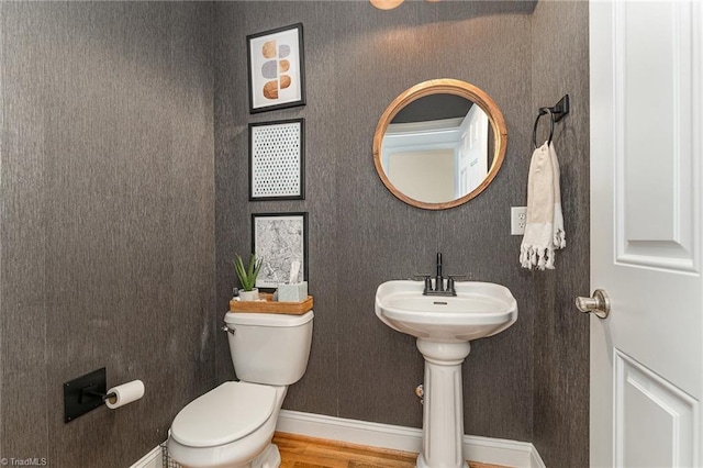 half bathroom with baseboards, toilet, and wood finished floors