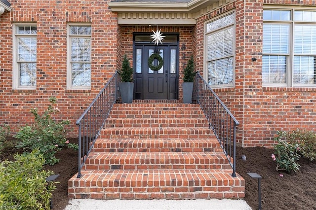 view of exterior entry with brick siding and a shingled roof