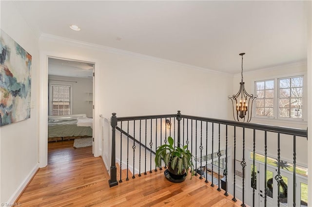 corridor with crown molding, a healthy amount of sunlight, wood finished floors, and a notable chandelier