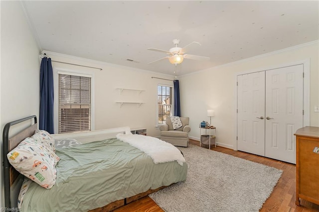 bedroom with ceiling fan, wood finished floors, baseboards, a closet, and crown molding