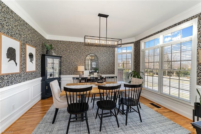 dining room featuring a wainscoted wall, ornamental molding, light wood-style flooring, and wallpapered walls