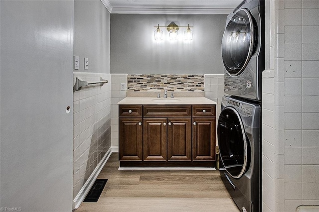 bathroom with tile walls, ornamental molding, wood-type flooring, stacked washer and dryer, and vanity