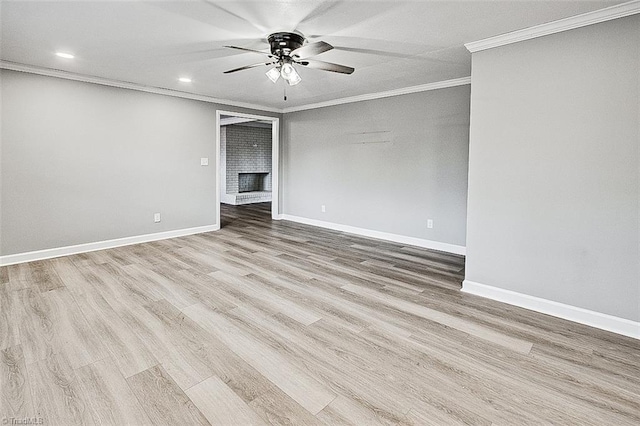 empty room featuring a fireplace, ceiling fan, crown molding, and light hardwood / wood-style floors