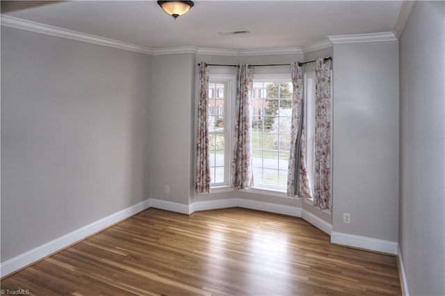 spare room with visible vents, ornamental molding, baseboards, and wood finished floors