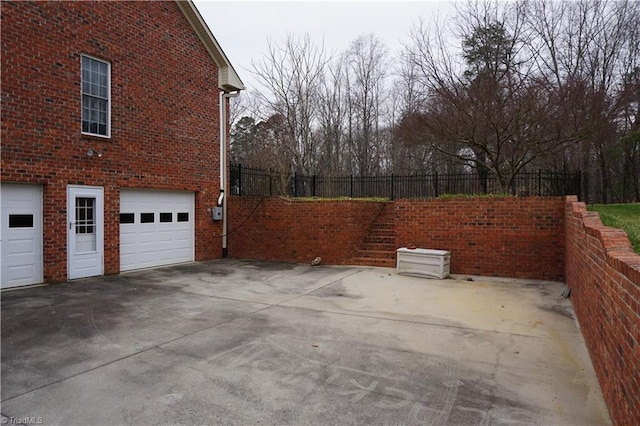 view of side of home with a garage, brick siding, concrete driveway, and fence