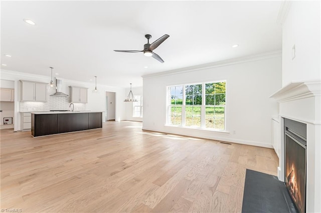 unfurnished living room featuring light wood finished floors, baseboards, a fireplace with flush hearth, ornamental molding, and ceiling fan with notable chandelier
