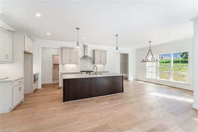 kitchen featuring light wood-type flooring, crown molding, wall chimney exhaust hood, and a kitchen island with sink