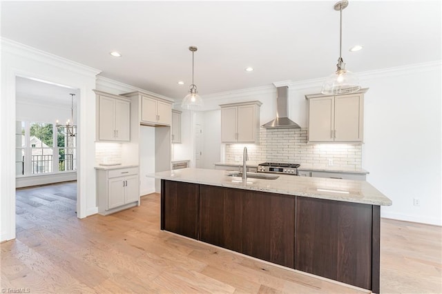 kitchen featuring a center island with sink, crown molding, wall chimney exhaust hood, and a sink