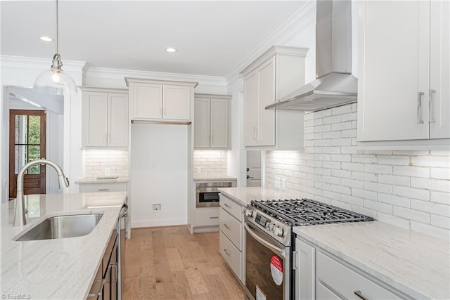 kitchen featuring light wood finished floors, crown molding, wall chimney range hood, gas range, and a sink