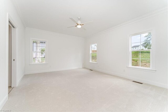 spare room with ornamental molding, light colored carpet, a wealth of natural light, and ceiling fan