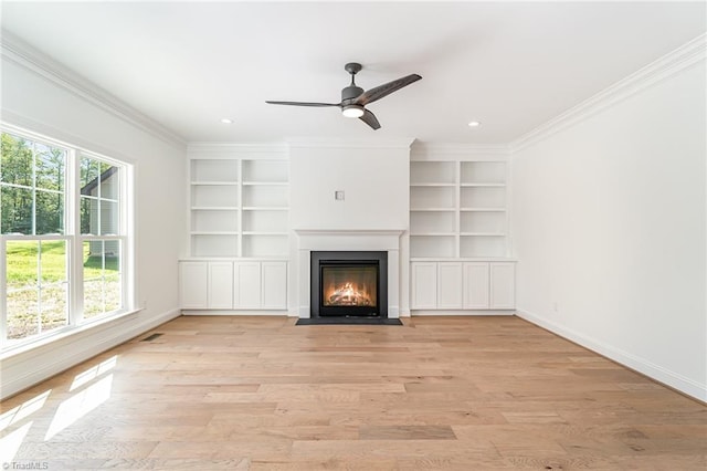 unfurnished living room with light wood-type flooring, built in features, ceiling fan, and crown molding