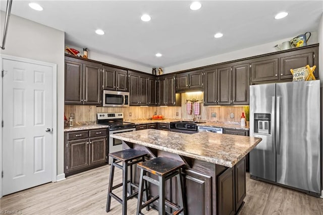 159 Forest Abbey Ln, China Grove, NC 28023 - kitchen with appliances with stainless steel finishes, light wood-type flooring, dark brown cabinetry, a center island, and a breakfast bar