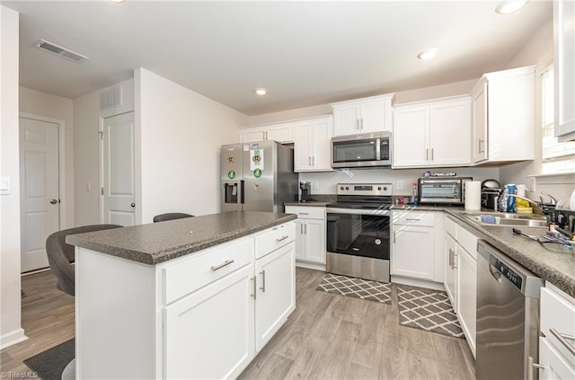 kitchen with a kitchen island, appliances with stainless steel finishes, white cabinetry, light hardwood / wood-style floors, and sink