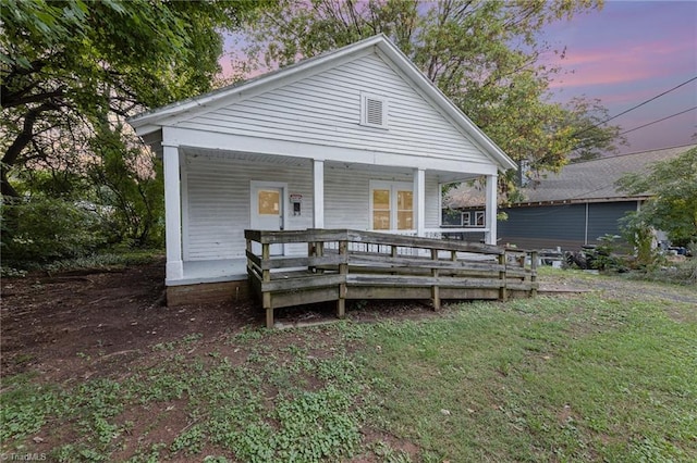 back house at dusk featuring a lawn and a porch