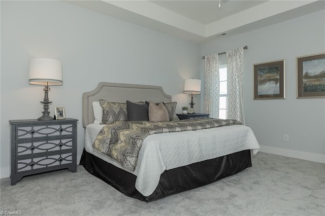 carpeted bedroom with a tray ceiling and baseboards