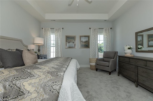 bedroom featuring light carpet, multiple windows, and a tray ceiling