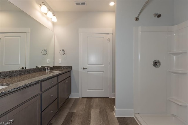 full bath featuring visible vents, walk in shower, double vanity, wood finished floors, and a sink