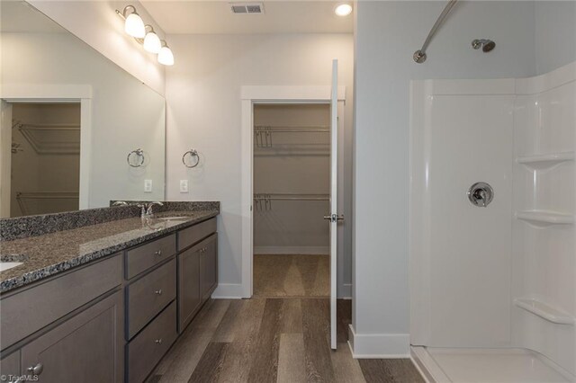 bathroom featuring visible vents, double vanity, wood finished floors, a shower, and a sink