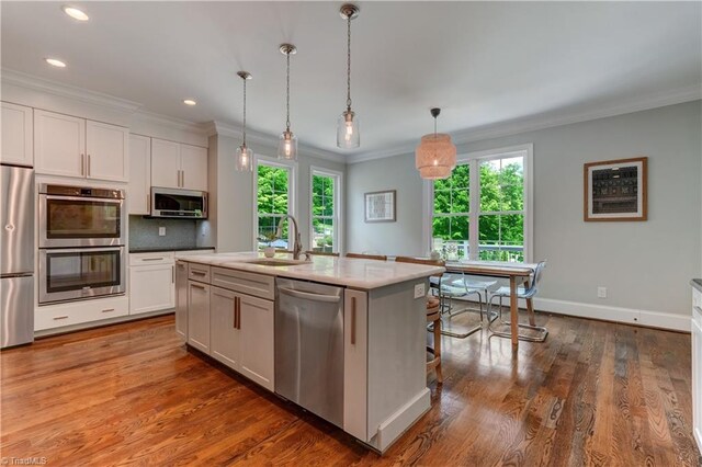 kitchen featuring stainless steel appliances, a sink, white cabinetry, healthy amount of natural light, and ornamental molding