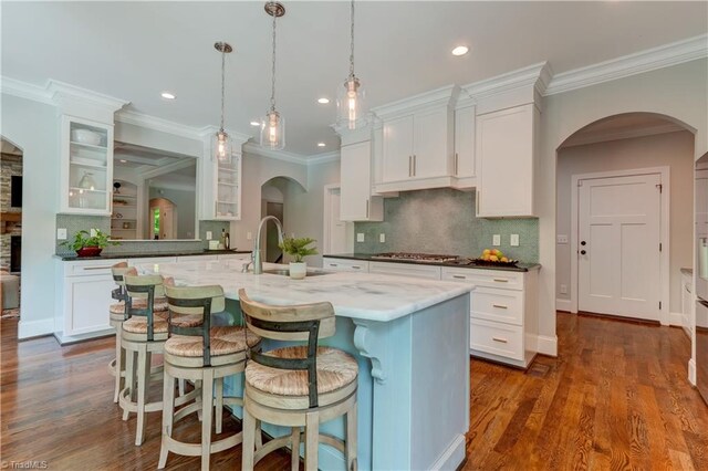 kitchen featuring stainless steel gas stovetop, a kitchen breakfast bar, glass insert cabinets, arched walkways, and recessed lighting