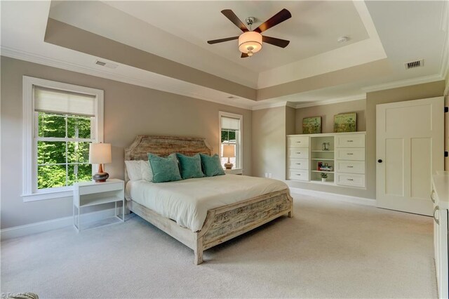 bedroom with a raised ceiling, light colored carpet, ornamental molding, baseboards, and ceiling fan
