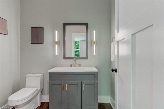 bathroom with toilet, vanity, wood finished floors, and baseboards