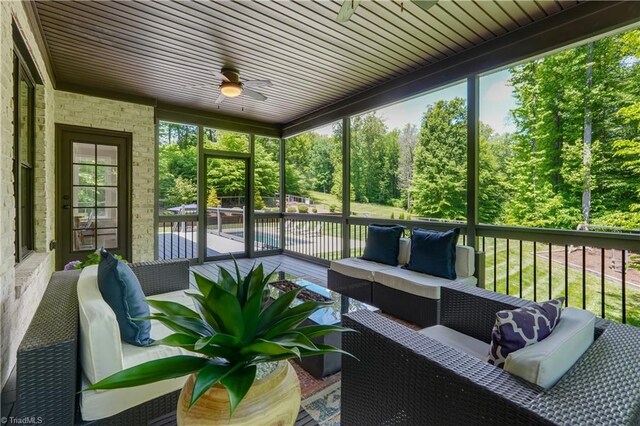 sunroom featuring an outdoor hangout area, ceiling fan, and view of scattered trees
