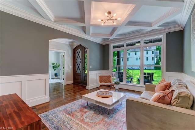 sitting room with arched walkways, a chandelier, crown molding, a decorative wall, and coffered ceiling